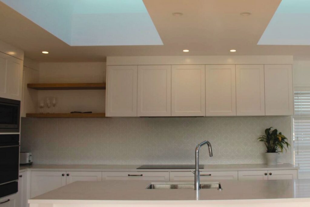 A modern kitchen with white cabinets, a large island with a sink, and two skylights illuminating the space.